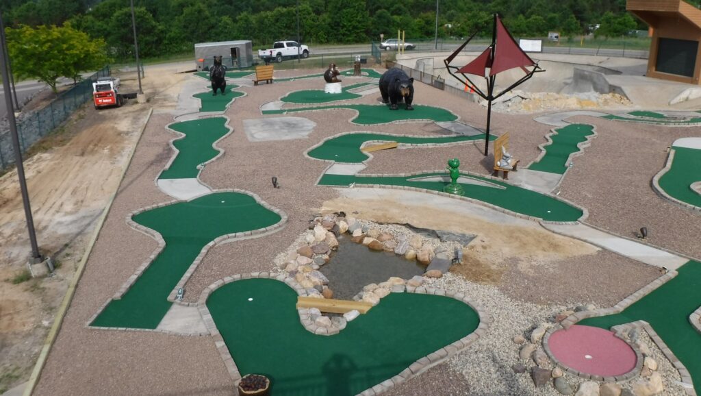 Miniature golf course with bear props, rocks, and wooden shoot-throughs, surrounded by gravel