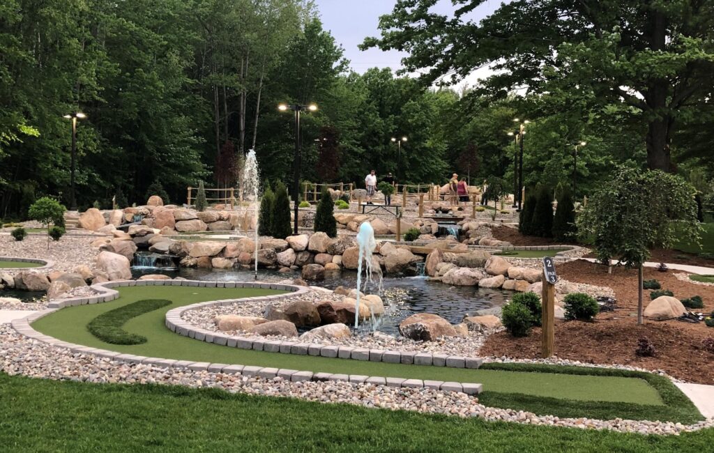 Miniature Golf course with water fountains throughout, trees in the background, and natural landscaping around the course