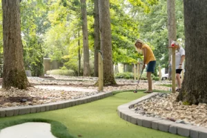 Player prepares her tee shot on a mini golf hole designed by AGS that winds around a forest of trees