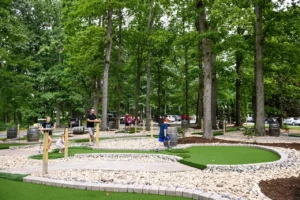 Dad watches his daughters tee up and his son walk to his first putt on this vineyard mini golf hole