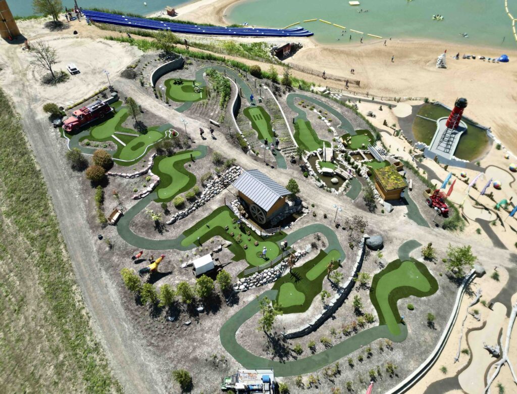 Miniature golf course placed along a hill, next to the beach. Water visible from the course, walkway in between the two sides of the course.