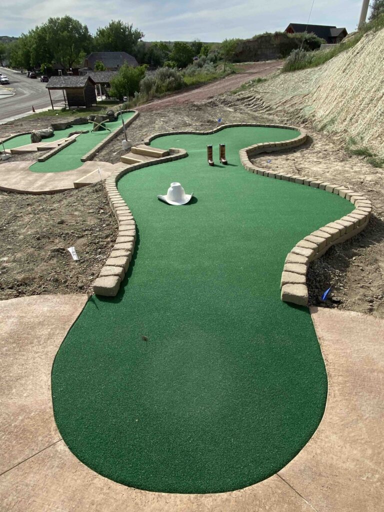 miniature golf course with cowboy props & obstacles, surrounded by dirt, each hole connected with cement walkthroughs