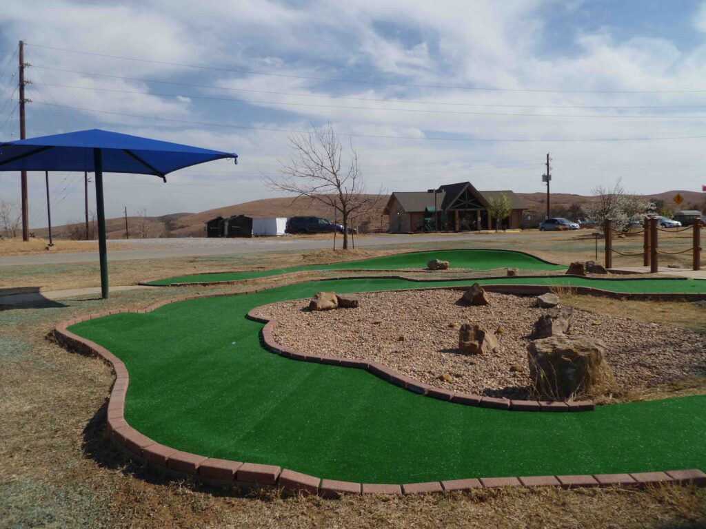 miniature golf course at an army base - blue umbrella aside course, green turf surrounded in dirt ground