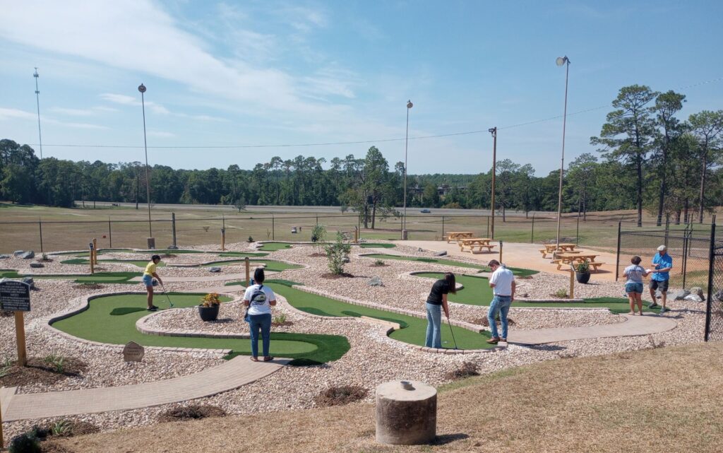 miniature golf course on flat land, people playing on the course. surrounded by natural gravel