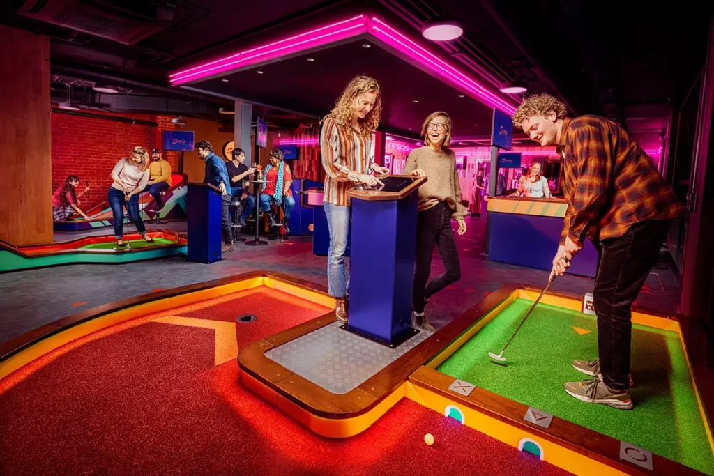 Woman enters her score into a console while a player watches his putt go through a barrier cut-out